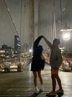 two people standing on a bridge in the rain with their hands up to each other