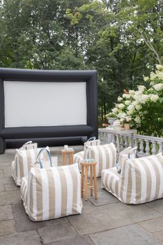 an inflatable movie screen is set up on the patio with striped pillows and stools