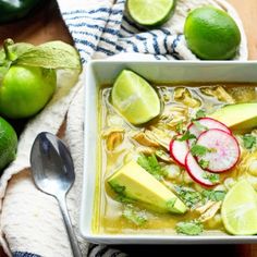 a bowl of soup with limes, radishes and avocado on the side