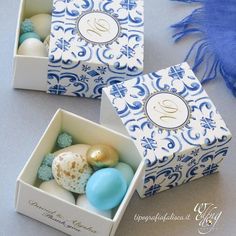 two boxes filled with blue and white decorated eggs next to a tassell scarf