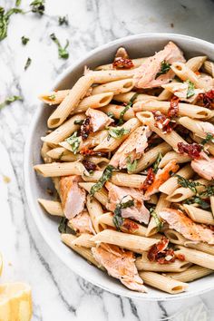 a white bowl filled with pasta and meat on top of a marble table next to lemon wedges