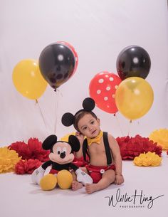 a little boy sitting in front of balloons and mickey mouse