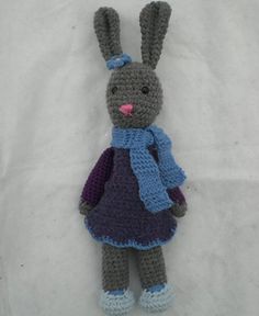 a crocheted stuffed rabbit wearing a purple dress and blue scarf with pink nose