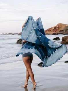 a woman is walking on the beach with her scarf over her head