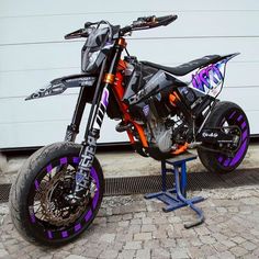 an orange and black dirt bike parked on top of a metal stand in front of a garage