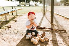 a little boy sitting on the ground with baseballs in front of him and wearing a red hat