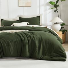 a bed with green sheets and pillows in a room next to a potted plant