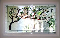 a stained glass window with white flowers and green leaves on the outside, hanging from a wall