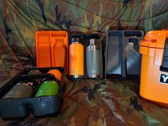 an orange and black lunch box with two water bottles in it next to other items