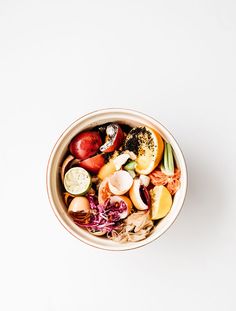 a bowl filled with lots of different types of fruits and veggies on top of a white surface