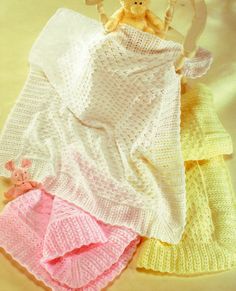 three knitted blankets and a teddy bear on a white surface with yellow, pink, and blue colors