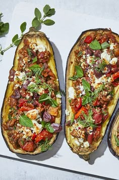 three stuffed eggplant halves on a cutting board with fresh herbs and feta cheese