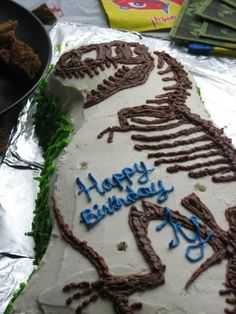 a birthday cake that looks like a dinosaur is on tin foil with chocolate chips in the background