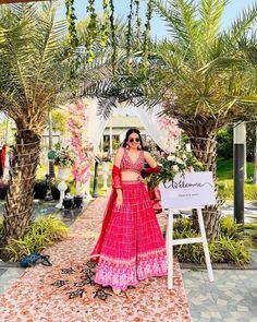 a woman in a red lehenga standing under a canopy with flowers and greenery