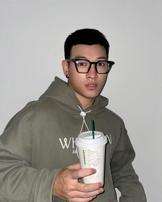 a young man wearing glasses holding a starbucks cup with a straw in it's mouth