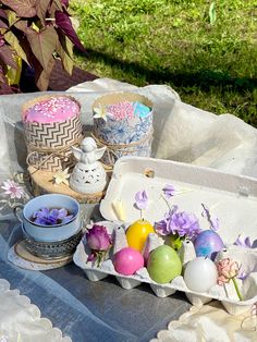 an assortment of decorated easter eggs and cupcakes sitting on a table in the grass