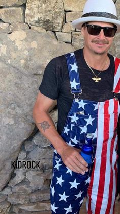 a man with an american flag apron and hat holding a water bottle in front of a stone wall