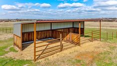 a horse barn with two stalls in the middle of a grassy field under a cloudy blue sky