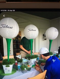 three people sitting at a table with golf balls on top of them and cups in front of them