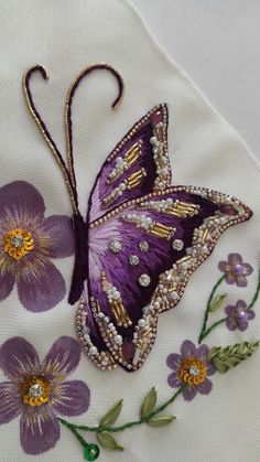 a purple butterfly is sitting on a white cloth with flowers and beads in it's wings