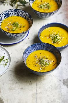 four bowls filled with soup and garnished with herbs sitting on a table next to plates