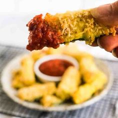 someone is holding up some food with sauce on the plate and dipping it in a small bowl