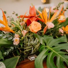 an arrangement of tropical flowers and greenery is displayed on a table at a wedding