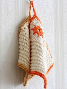 an orange and white crocheted towel hanging from a hook on the side of a wall