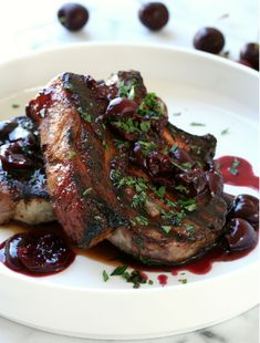 a white plate topped with meat covered in sauce and garnished with cherries