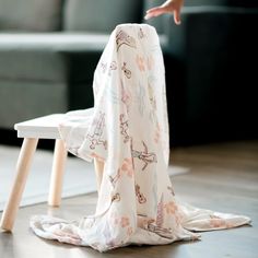 a baby's blanket on the floor next to a wooden table with a person reaching for it