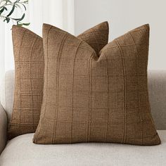 two brown pillows sitting on top of a couch next to a vase filled with flowers