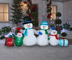 three snowmen in front of a house decorated for christmas