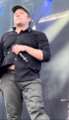 a man standing in front of a stage holding a microphone and wearing a baseball cap