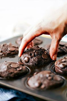 a person picking up a chocolate cookie from a muffin tin