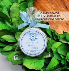 a candle that is sitting on top of some green leafy plants and has a blue ribbon around it