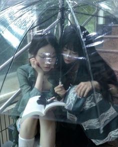 two women are sitting under an umbrella and reading