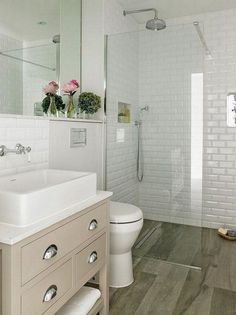 a white bathroom with wooden floors and tile walls, along with a walk in shower