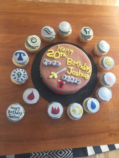 a birthday cake with cupcakes around it on top of a wooden table,