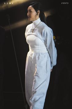 a woman in white outfit standing on stage with microphone behind her back to the camera