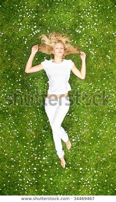 a woman laying in the grass with her hair flying through the air and looking up