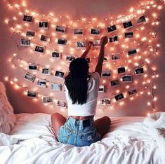 a woman sitting on top of a bed in front of a string of lights