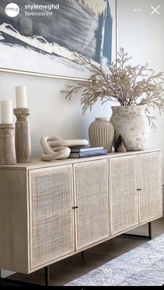 a white vase sitting on top of a wooden cabinet next to a painting and candles