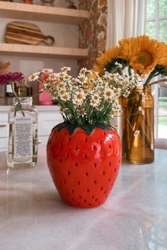 a strawberry shaped vase sitting on top of a counter next to other vases filled with flowers