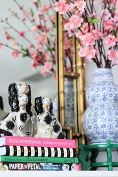 two black and white dog figurines sitting on top of books in front of a vase with pink flowers