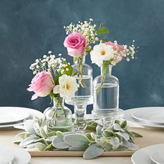 the table is set with white and pink flowers in vases, plates, and silverware