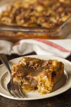 a piece of bread pudding on a plate with a fork and casserole dish in the background