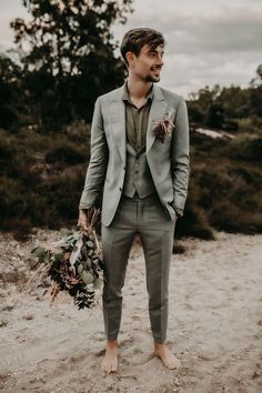 a man in a gray suit holding a bouquet and looking off to the side with trees in the background