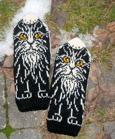 two knitted black and white cat mittens sitting on top of snow covered ground