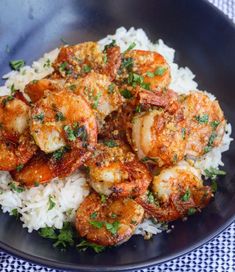 a black plate topped with rice and shrimp on top of a blue checkered table cloth