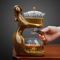 a person is pouring something into a glass cup on top of a wooden table with an object in the shape of a woman's head